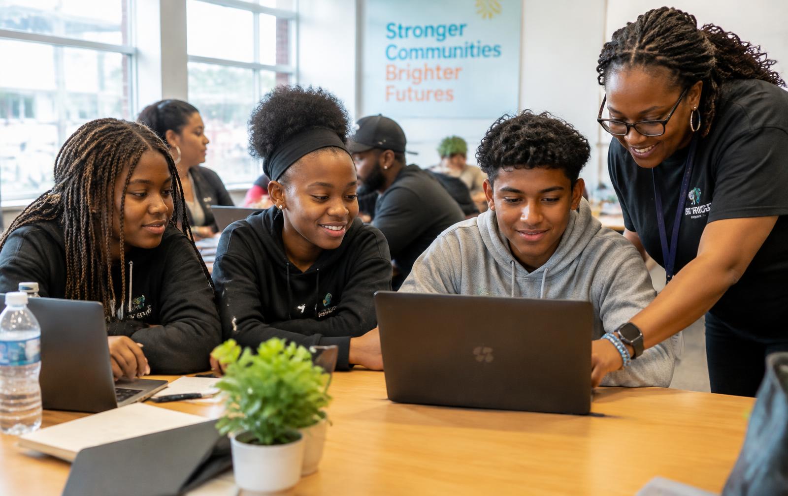Youth and a mentor learning together on laptops in a community classroom
